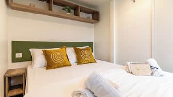 Una cama bien hecha con dos almohadas, una mesita de noche, un estante de madera sobre la cama y una toalla en la cama.