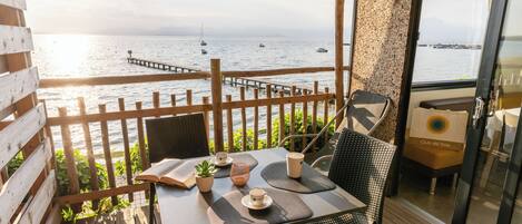 A wooden deck with a table and chairs, overlooking a body of water with boats and a pier.