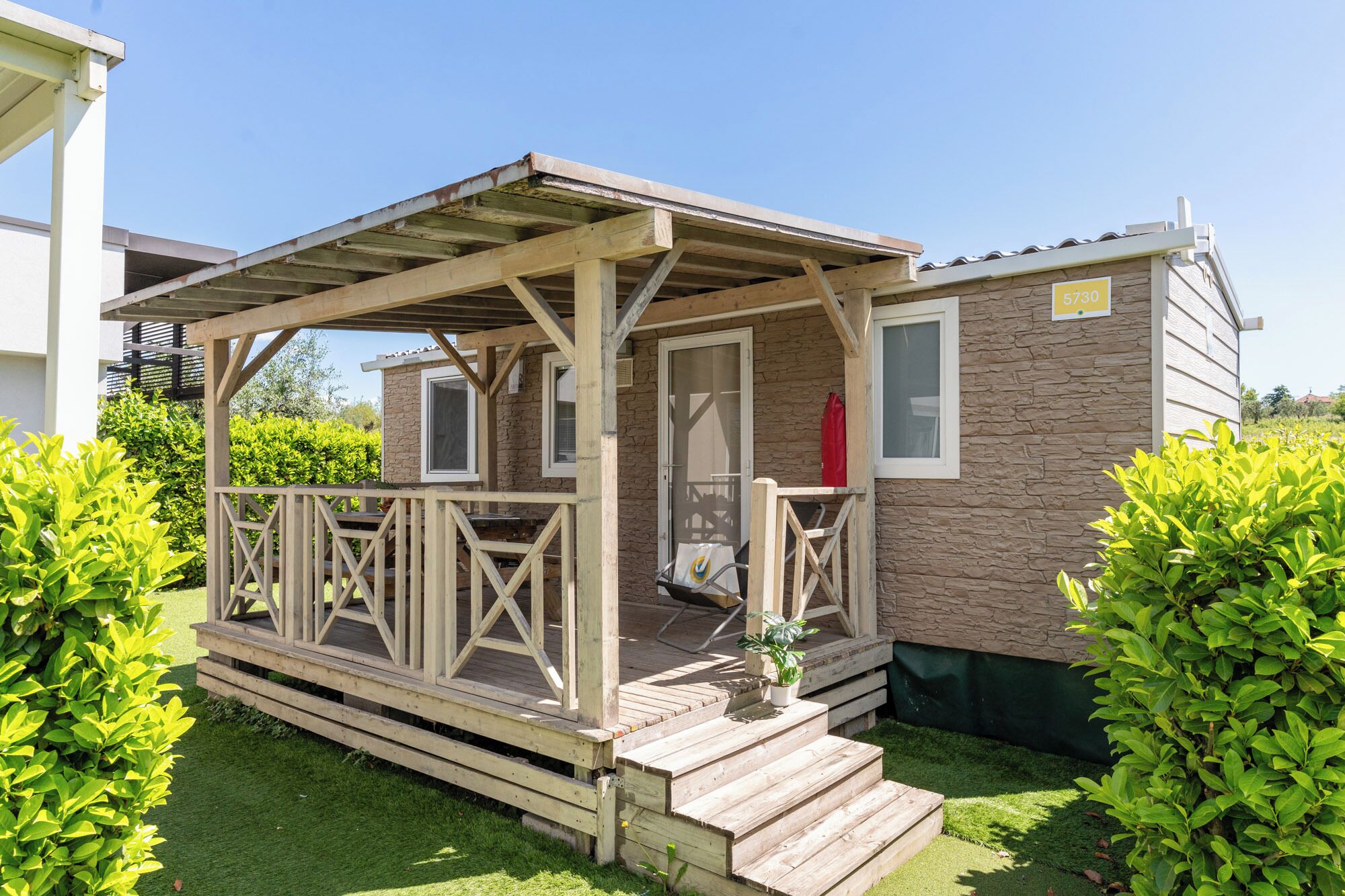Een kleine, gelijkvloerse stacaravan met een houten terras en een overdekte veranda.
