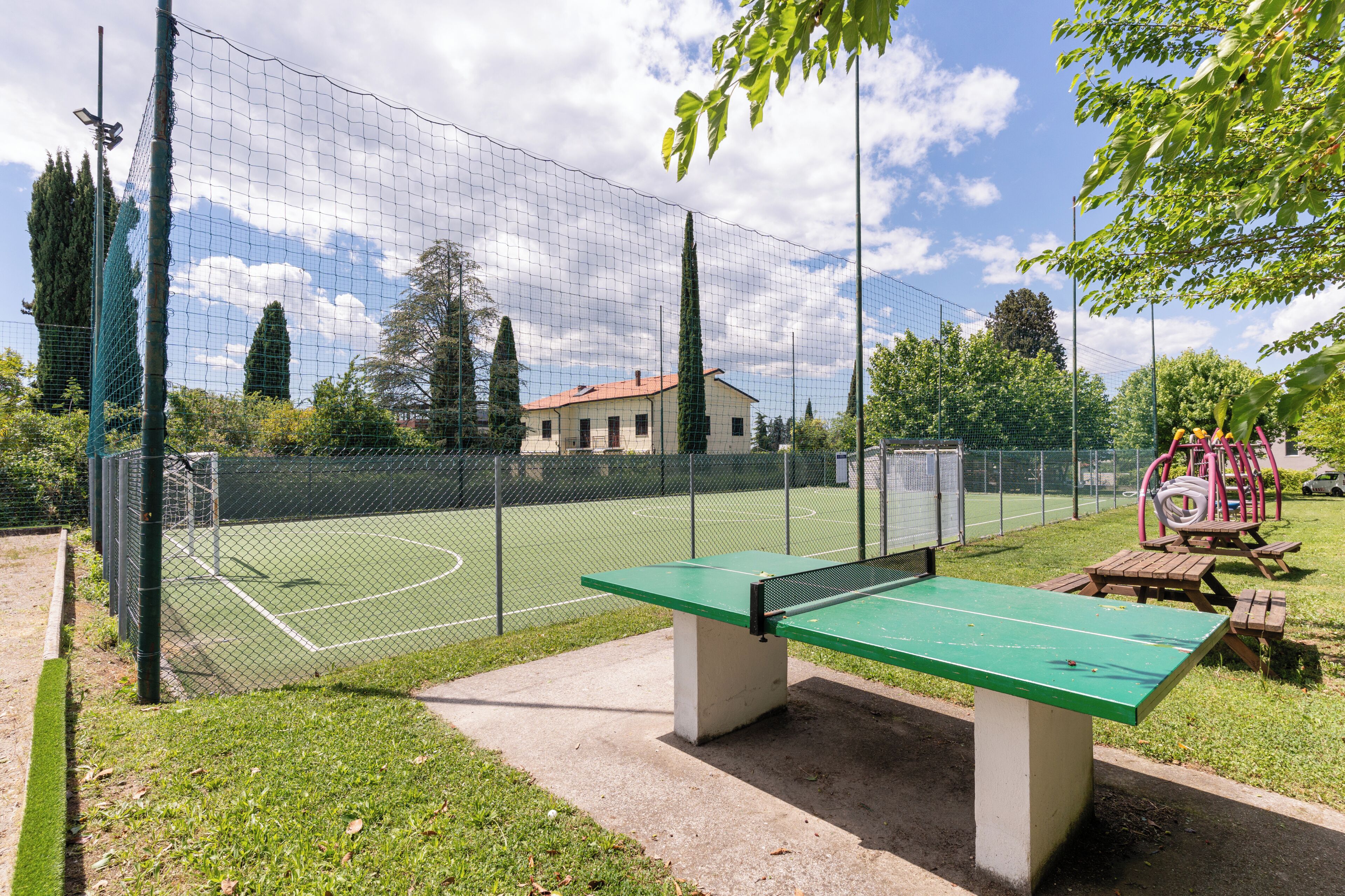 A tennis court with a net, a green bench, and a playground with swings and slides.