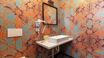 Un bagno con parete decorata, lavandino bianco, asciugacapelli e una piccola pianta.