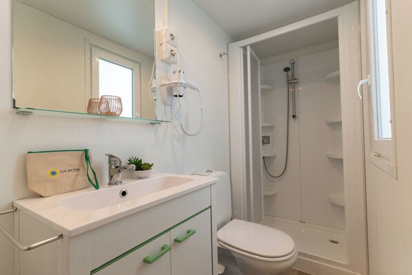 Un bagno con un lavandino bianco, un water, cabina doccia in vetro e uno specchio con ripiano sopra.