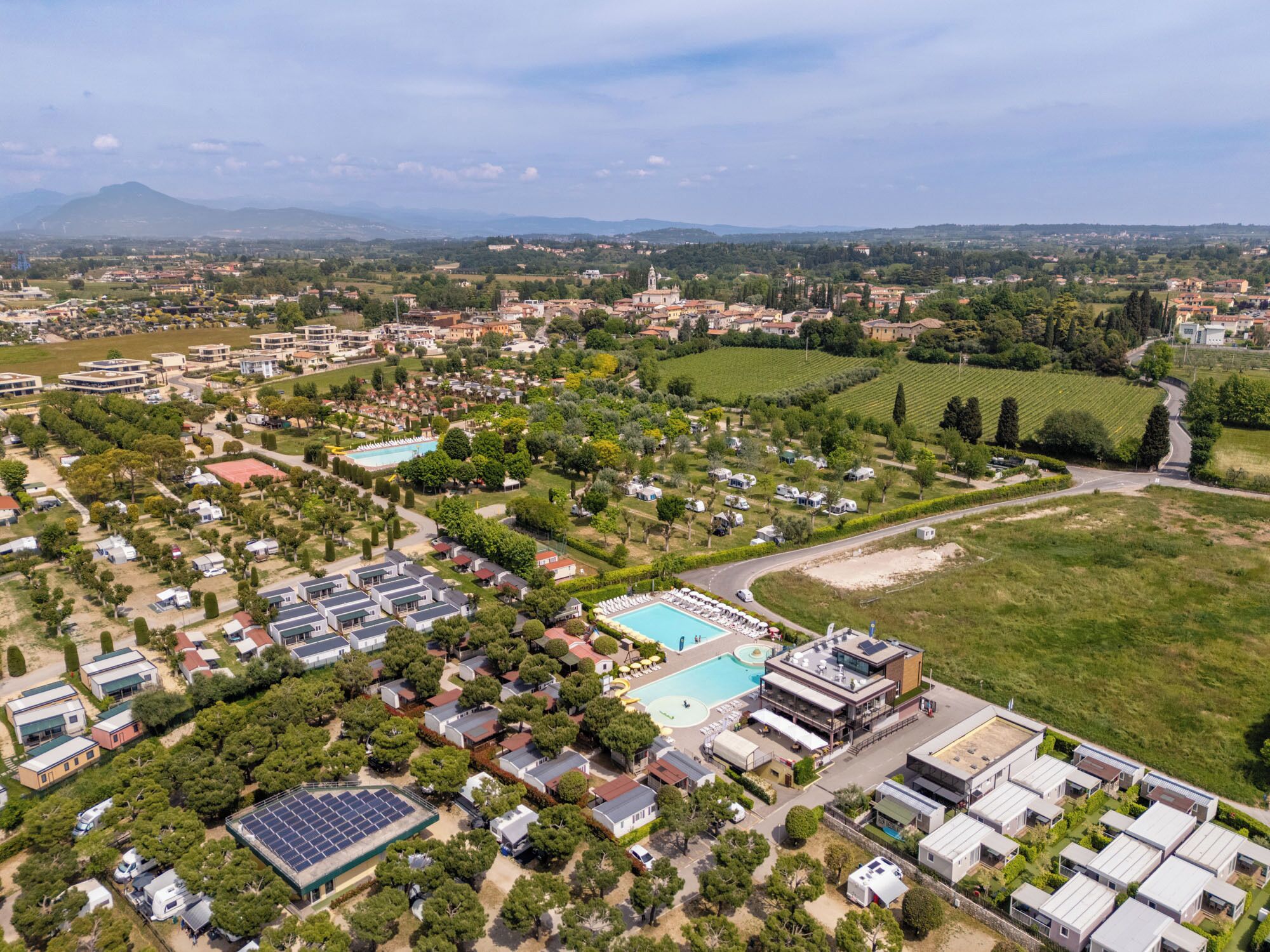 An aerial view of a residential area with multiple buildings, a swimming pool, and green fields.
