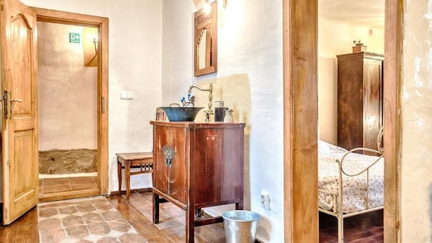 Un bagno rustico con un armadietto in legno, un lavabo e un letto nella stanza adiacente.