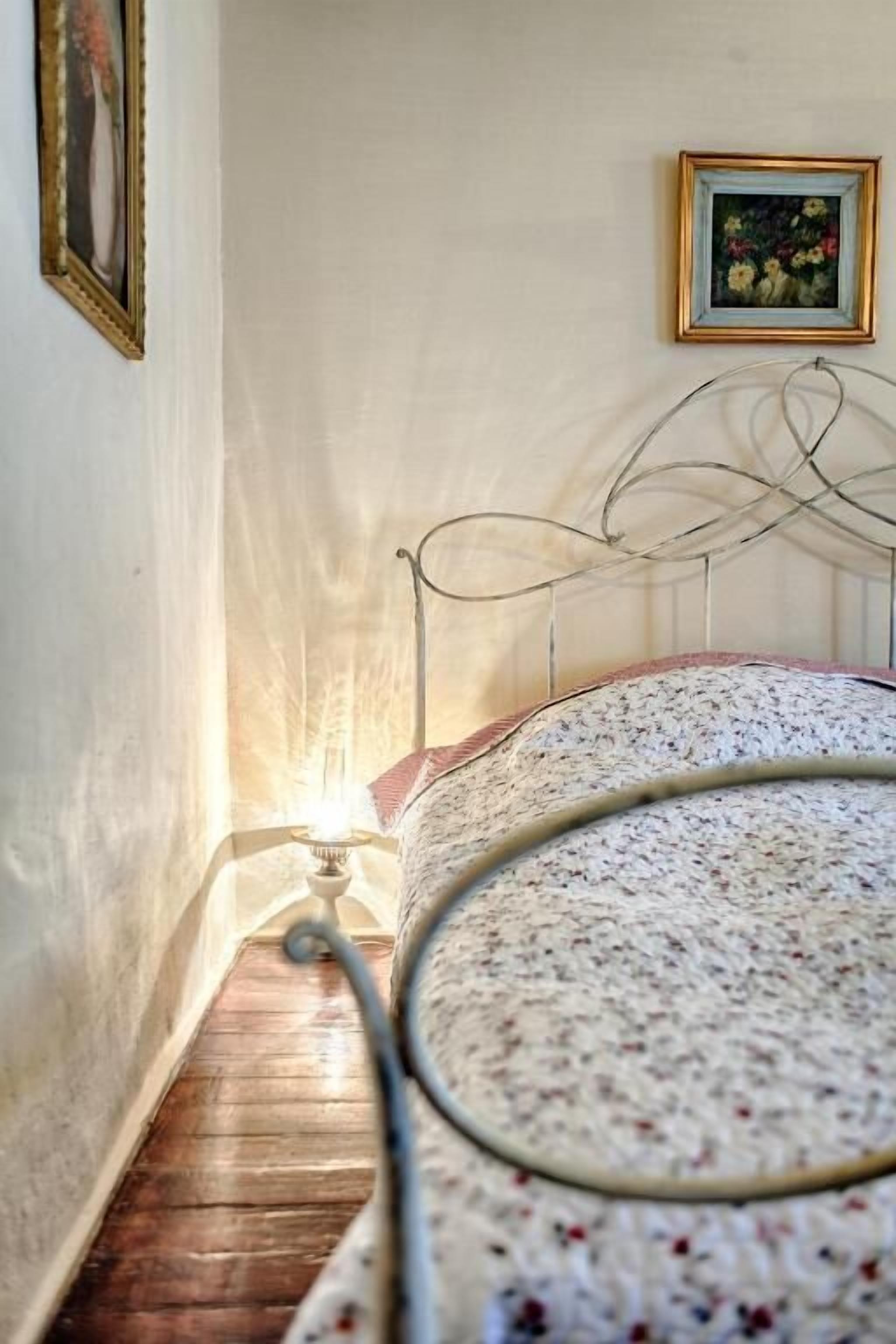 Un couloir étroit, avec un lit au fond, un tableau encadré au mur et une lampe sur la table de chevet.