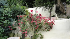 Un giardino con un muro bianco, due tavoli rotondi con piani in mosaico e un cespuglio fiorito.