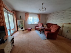 A living room with a sofa, armchairs, a coffee table, a television, and a cabinet.