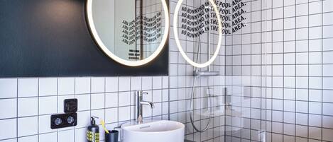Un baño moderno con un espejo redondo, un lavabo y una ducha.