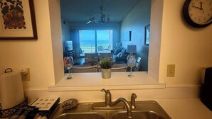 A kitchen with a view of a living room, a dining area, and a balcony with a view of the ocean. - Rock the Sunset – Palm Coast Condo (Palm Coast)