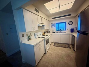 Eine moderne Küche mit weißen Schränken, einem Edelstahlkühlschrank, einem Einbauofen und einem Fenster mit Blick auf den Balkon.