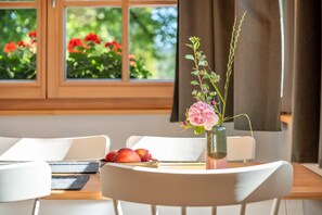 A dining table with a vase of flowers, a plate of fruit, and a view of a garden through a window. - Schwarzwaldgrün Holiday Apartment (Bonndorf im Schwarzwald)
