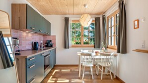 Une cuisine avec des meubles de rangement en bois, une table à manger avec des chaises et une fenêtre avec des rideaux.