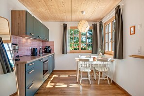 A kitchen with wooden cabinets, a dining table with chairs, and a window with curtains. - Schwarzwaldgrün Holiday Apartment (Bonndorf im Schwarzwald)