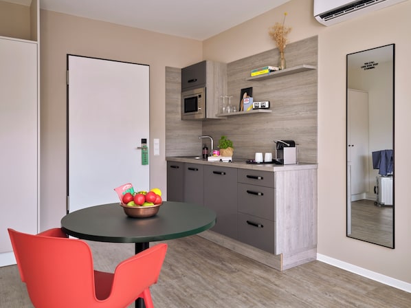 Una cucina moderna con zona pranzo, caratterizzata da un tavolo rotondo, sedie rosse e una ciotola di frutta.