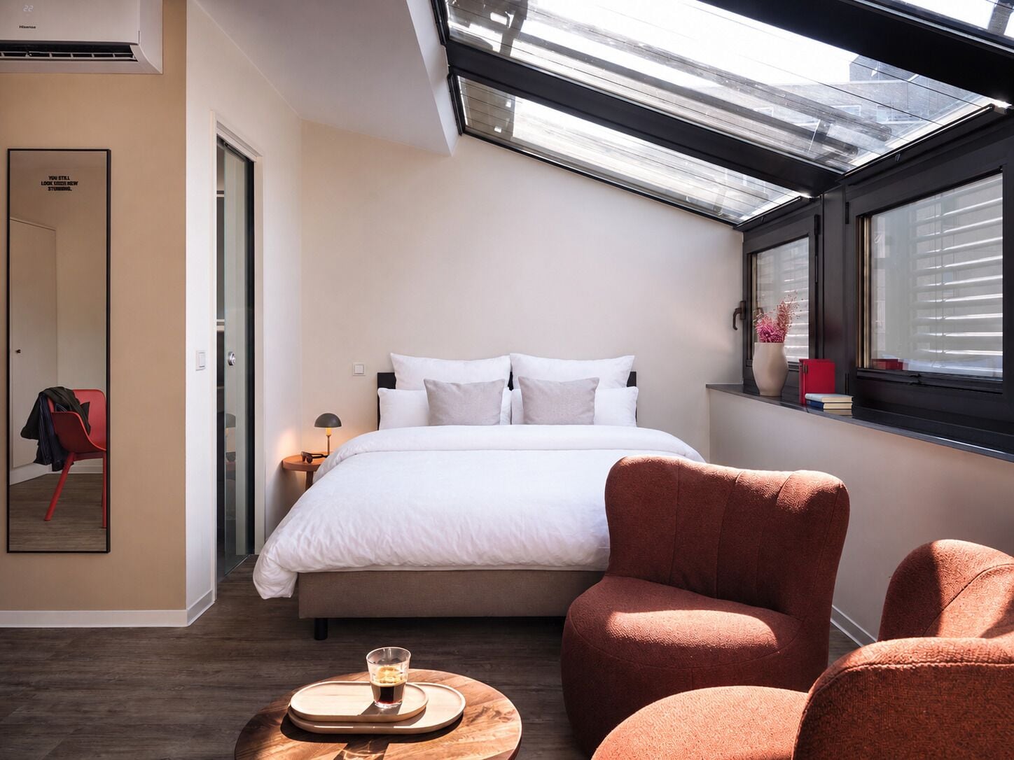 Une chambre d’hôtel moderne dotée d’une lucarne, d’un lit, d’un coin salon et d’une table d’appoint avec une boisson.