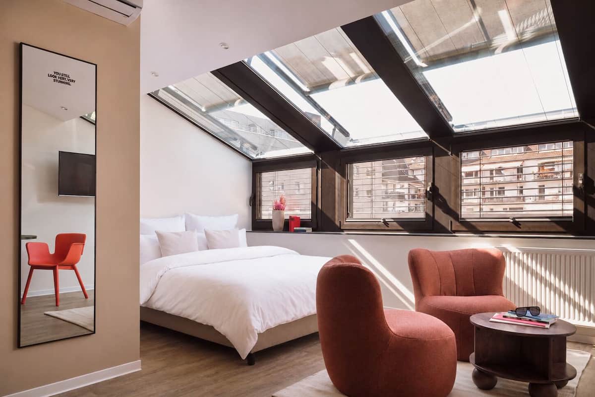 A modern bedroom with a skylight, a bed, a red chair, and a small table.