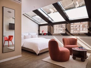 Una camera da letto moderna con un lucernario, un letto, una sedia rossa e un tavolino.
