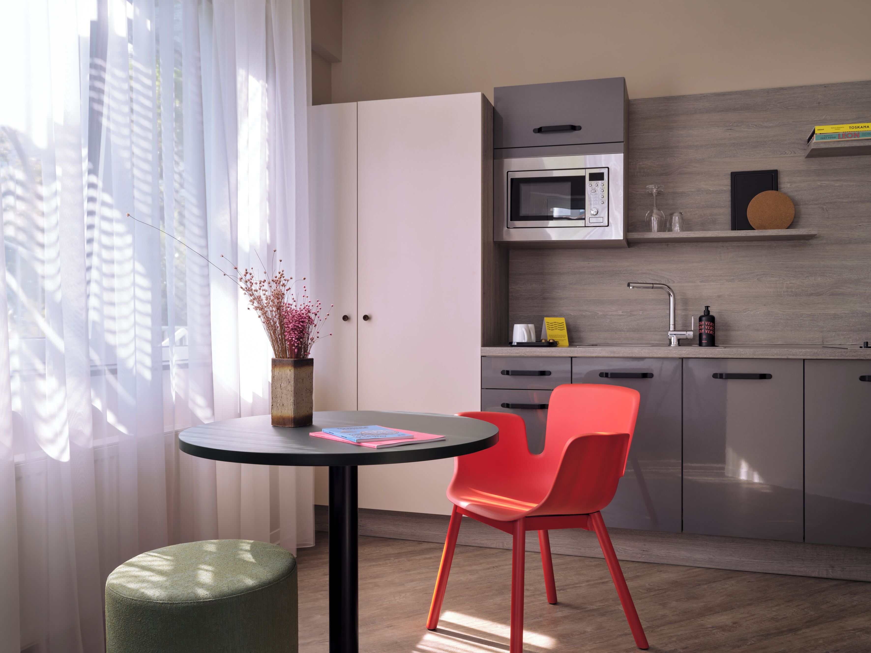 A modern kitchen with a microwave, sink, and cabinets. There is a round table with a chair and a vase with flowers.