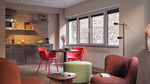 A modern living room with red chairs, a green ottoman, and a wooden coffee table. - STAYERY Cologne Sülz (Cologne)