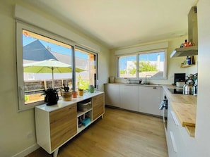 Eine moderne Küche mit weißen Schränken, Holz Arbeitsplatten und großen Fenstern mit Blick nach außen.