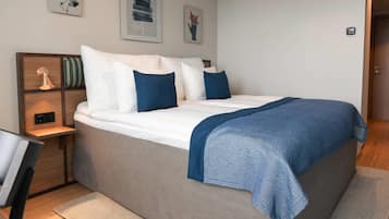 A neatly made bed with a blue blanket, a wooden bedside table with a lamp, and a wall-mounted light switch.