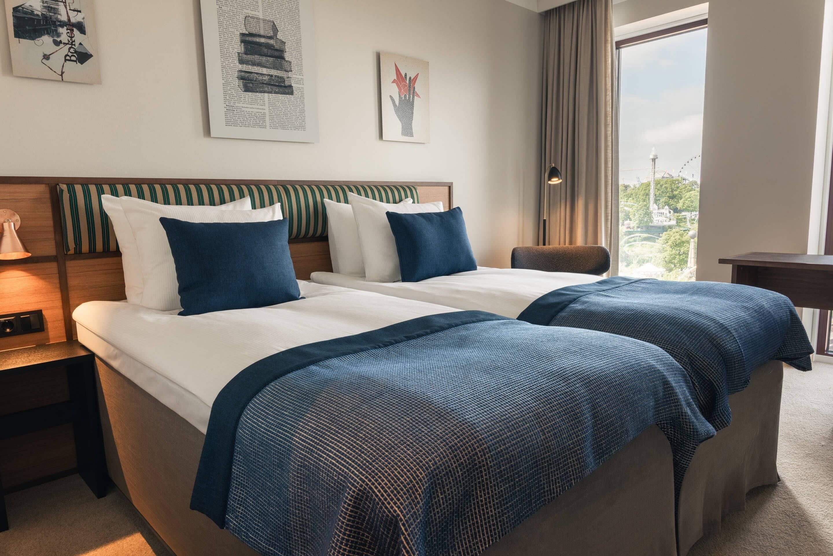 Une chambre d’hôtel avec deux lits, une table de chevet, une chaise, un bureau et une grande fenêtre donnant sur une grande roue.