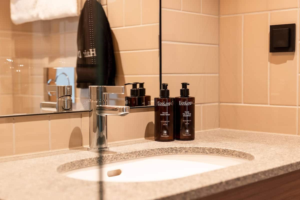 Ein Badezimmer mit einem Waschbecken, zwei Shampoo-Flaschen, einem Handtuch und einem Spiegel.