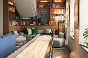 A cozy living room with a shuffleboard table, bookshelves, a sofa, and a lamp. - Quality Hotel The Book (Gothenburg)