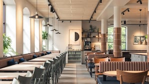Un interior de restaurante moderno con mesas comunes largas, cabinas individuales e iluminación colgante.