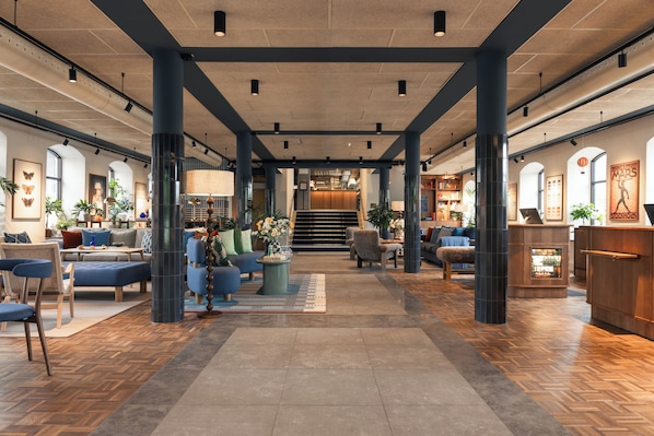 A spacious lobby with a central staircase, seating areas, and a reception desk.