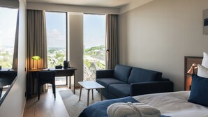Habitación de hotel con cama, escritorio, sillón, sofá y vistas a la ciudad.