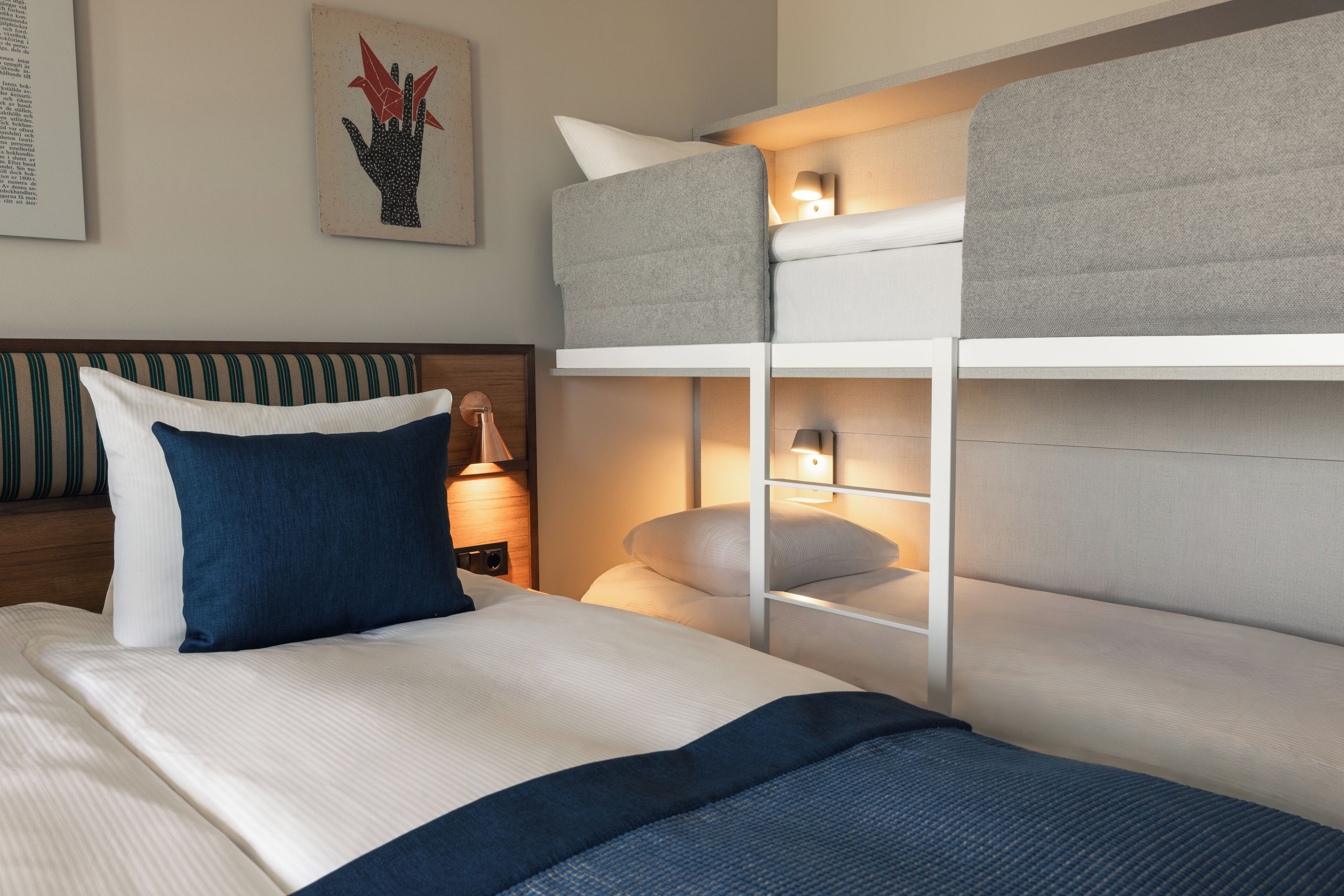 Habitación de hotel con literas, una lámpara de noche, una obra de arte enmarcada en la pared y un cojín a rayas.