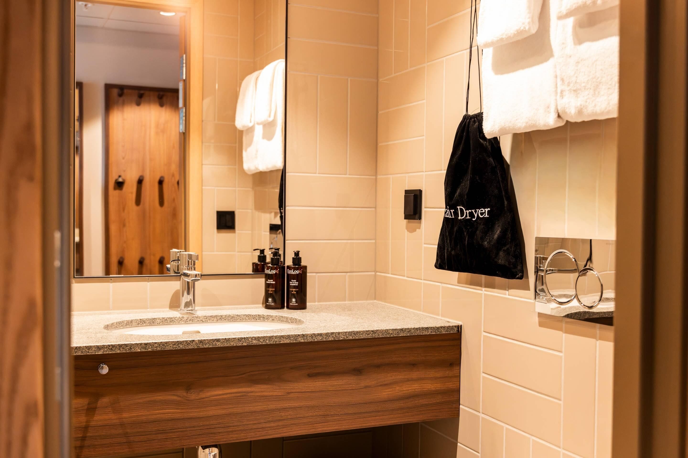 Un baño con tocador de madera, un espejo, un perchero y un bolso negro con la etiqueta 'air Dryer'.