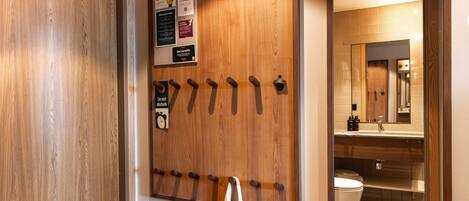A wooden wall with a coat hook, a bulletin board with notices, and a bathroom visible through a mirror.