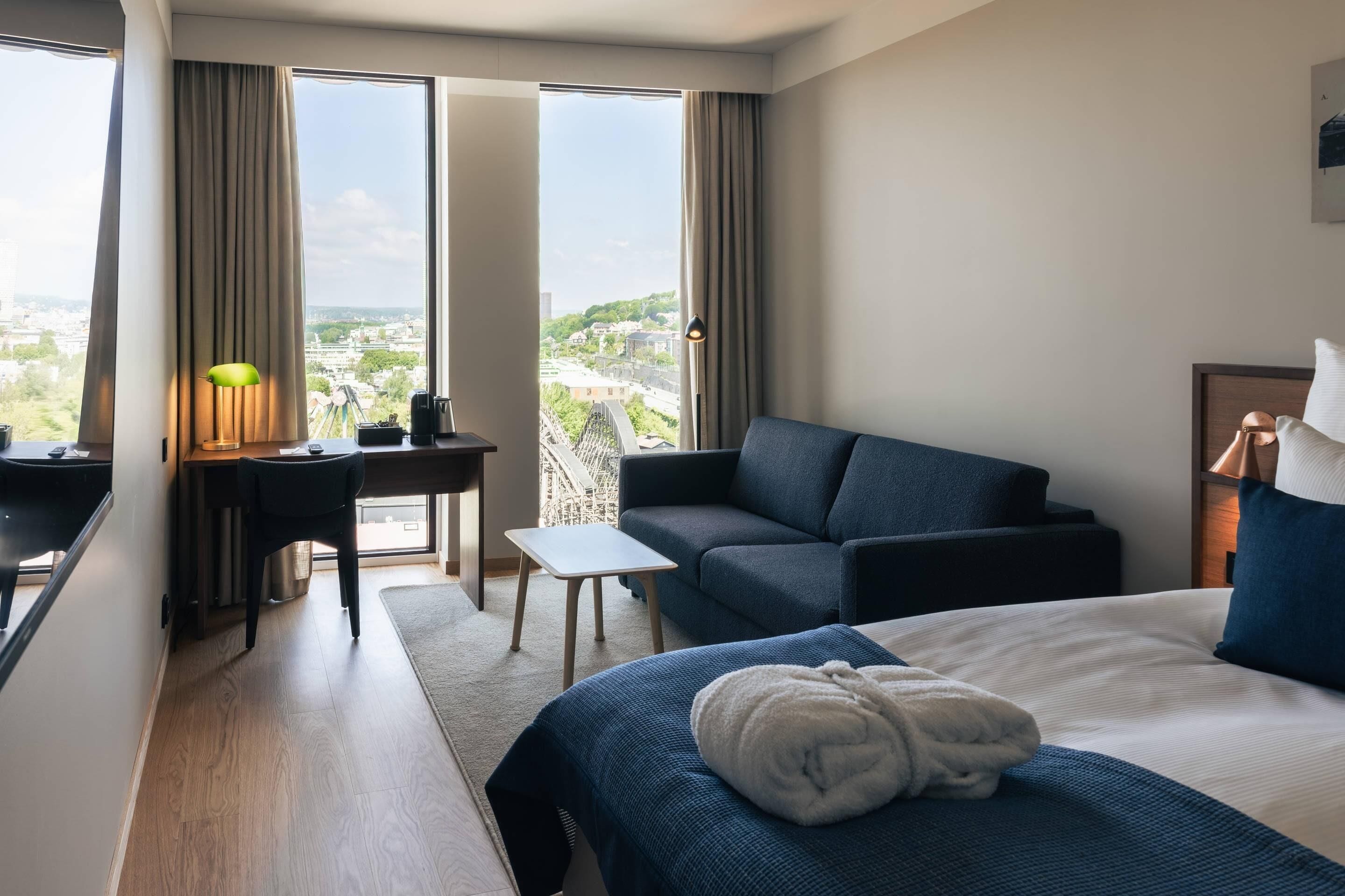 Habitación de hotel con cama, escritorio, sofá y vista a la ciudad.