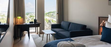 Habitación de hotel con cama, escritorio, sofá y vista a la ciudad.