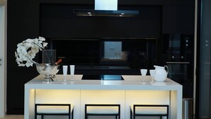 A modern kitchen with a central island, three bar stools, a stainless steel range hood, and a vase with white flowers. - The Breeze of Carthage Earthly Paradise (Carthage)