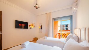 Une chambre d’hôtel avec deux lits, un téléviseur affichant « NETFLIX », un balcon avec une table et des chaises, et une vue sur les bâtiments.