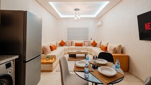 Un espace de vie compact comprenant un coin cuisine, un ensemble de canapés, une table à manger et un luminaire au plafond.