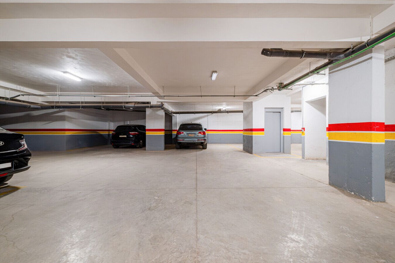 Eine Tiefgarage mit zwei Autos, Betonböden und Säulen mit roten, gelben und grauen Streifen.