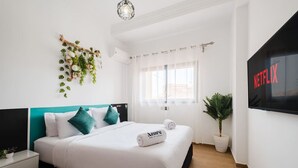 Moderni hotellihuone, jossa on sänky, televisio, ikkuna ja seinälle kiinnitetty kasvi.