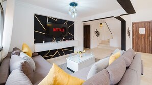 Moderni olohuone, jossa on suuri litteänäyttöinen televisio, portaikko ja minimalistinen sisustus.