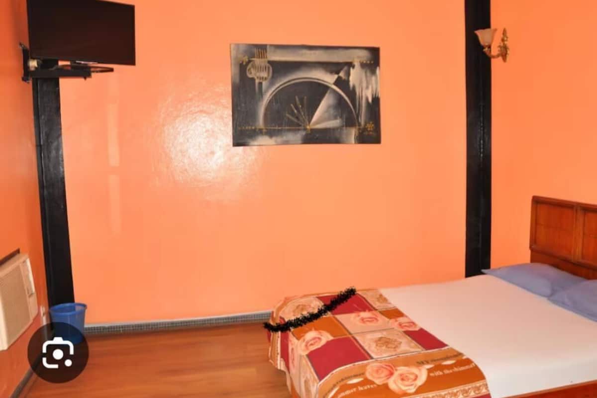 Una habitación con una cama, un televisor montado en la pared y un cuadro enmarcado.