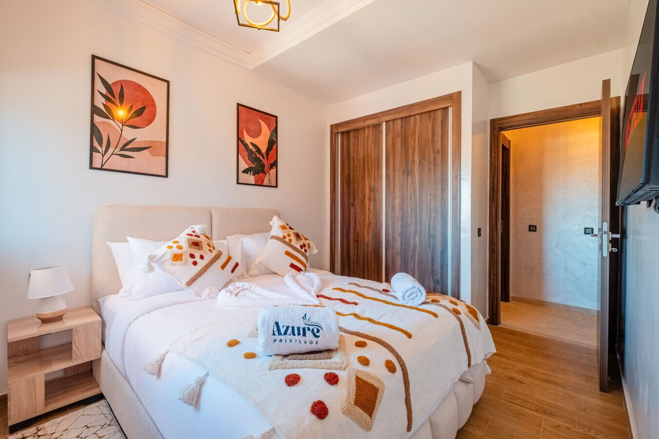 Una habitació d'hotel amb un llit gran, una tauleta de nit, un armari de fusta i dues obres d'art emmarcades a la paret.