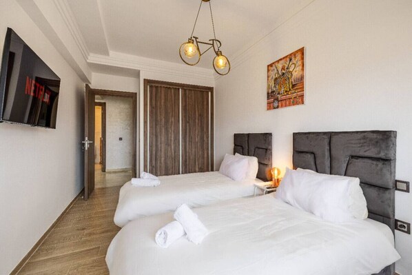 Habitación de hotel con dos camas, un armario de madera, un cuadro en la pared y un televisor a la izquierda.