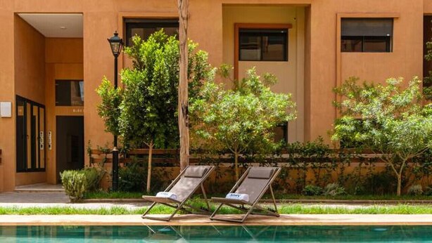 A swimming pool with lounge chairs, surrounded by a building with multiple windows and a door. - Guéliz 2BR Near M Avenue – Piscine, Balcons & Clim (Marrakesh)