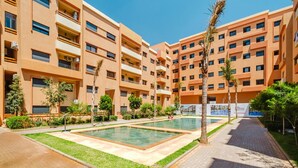 A multi-story hotel with a swimming pool, outdoor seating, and palm trees. - 2 min M-avenue / Guéliz Clim, Piscines & Parking (Marrakesh)