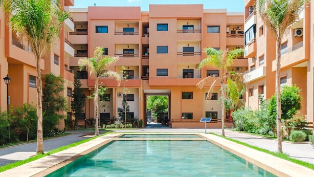 A modern building with a central pool, surrounded by greenery and palm trees. - 2 min M-avenue / Guéliz Clim, Piscines & Parking (Marrakesh)