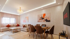 A modern living room with a sofa, coffee table, dining table with chairs, and artwork on the walls. - 2 min M-avenue / Guéliz Clim, Piscines & Parking (Marrakesh)