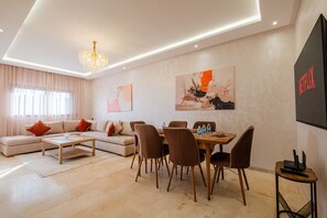 A modern living room with a sofa, coffee table, dining table with chairs, and artwork on the walls. - 2 min M-avenue / Guéliz Clim, Piscines & Parking (Marrakesh)